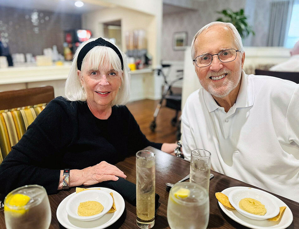 Senior residents enjoy a meal together at a dining table inside a senior living community restaurant.